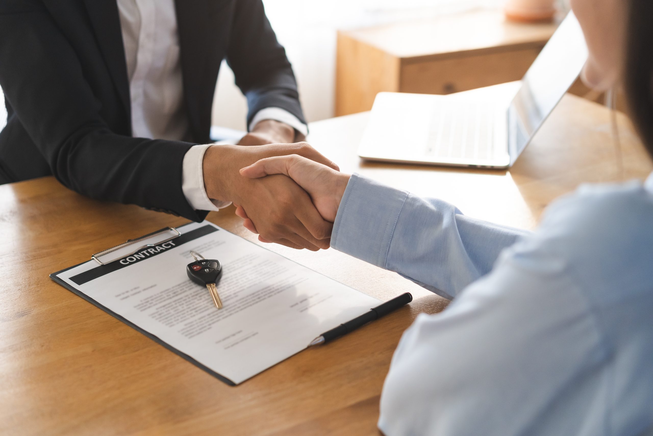 Two people finalizing an agreement with a handshake over a desk that holds a contract, symbolizing the new hybrid rental deposit model being offered by Firstcaution in the Swiss market.