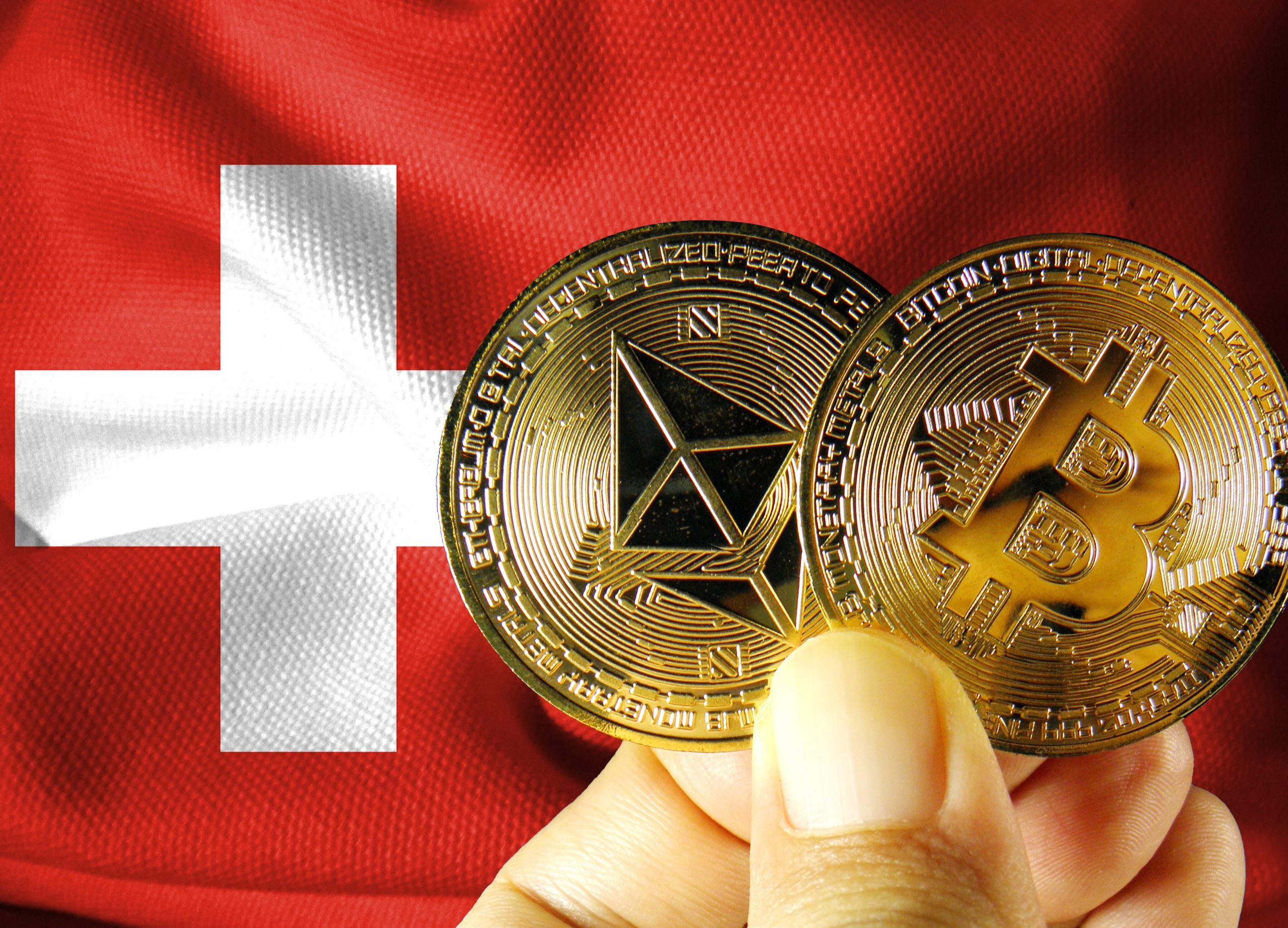 A hand holding gold Bitcoin and Ethereum coins against a background of the Swiss flag.