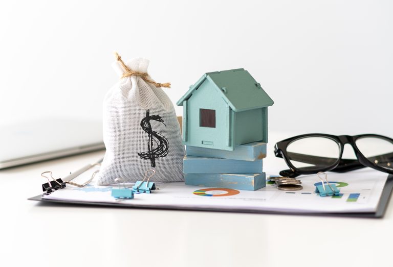 A conceptual image representing wealth management, showing a money bag, a miniature house, and eyeglasses resting on financial charts. The scene symbolizes the management of various assets, which is the core subject of the article about challenges for Swiss wealth managers.