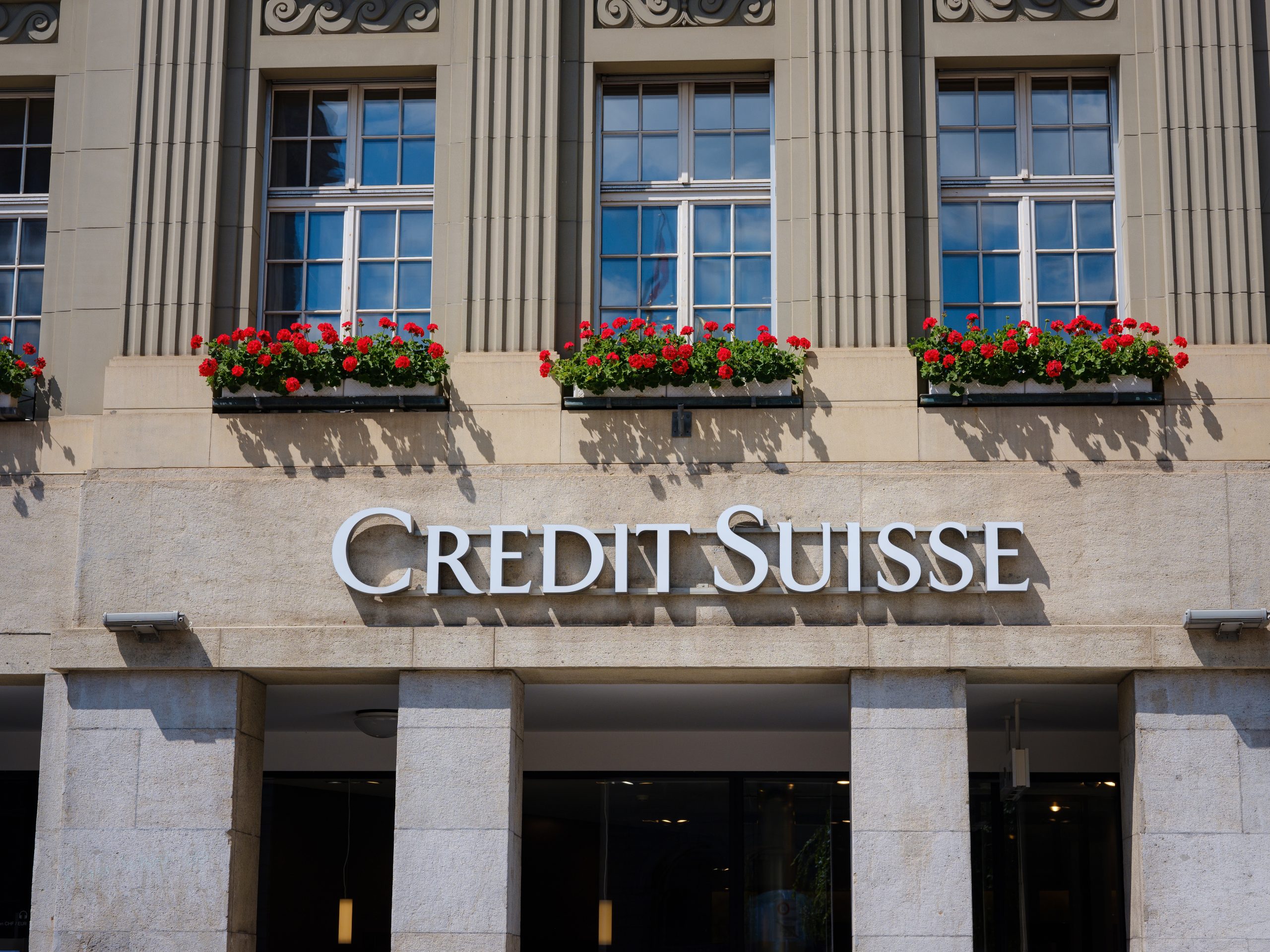 The exterior of a Credit Suisse bank branch, a major Swiss bank, is shown on a sunny day. The image is used in an article discussing the Swiss banking sector's challenges and the debate over new regulations following recent financial crises.