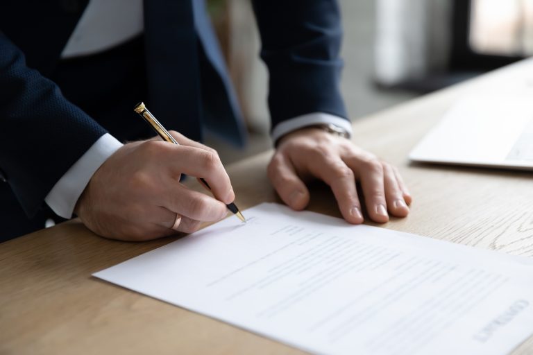 A close-up of a person in a business suit signaling a contract on a wooden desk. The image symbolizes the formation of a new business deal, representing the partnership discussed in the article.