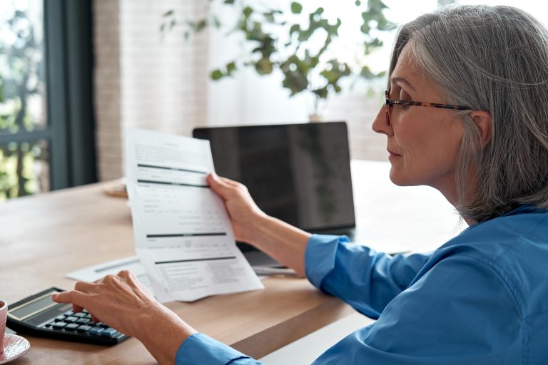 A mature woman sits at a desk, reviewing financial documents and using a calculator, with a laptop nearby. The image represents the act of personal retirement planning, a process that, as the 2025 article discusses, is being revolutionized by digital tools.