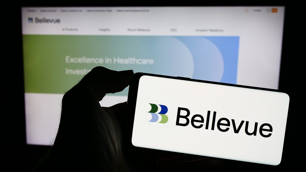 A smartphone displays the logo for Bellevue Group, with the company's website visible in the background highlighting its focus on healthcare investing. The image represents the asset manager at the center of a 2025 article about its strategic decision to divest a subsidiary and concentrate on its core healthcare business.