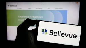 A smartphone displays the logo for Bellevue Group, with the company's website visible in the background highlighting its focus on healthcare investing. The image represents the asset manager at the center of a 2025 article about its strategic decision to divest a subsidiary and concentrate on its core healthcare business.