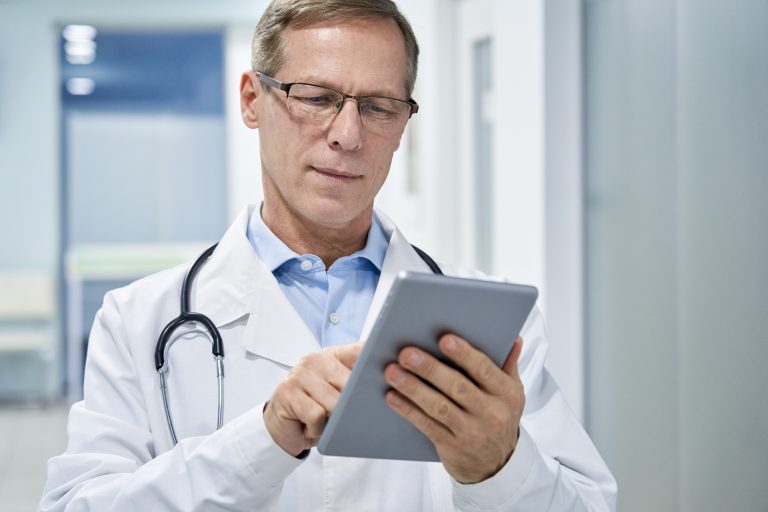 A healthcare professional in a white coat uses a digital tablet, representing the intersection of medicine and technology.