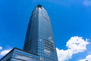 A low-angle shot of the Goldman Sachs headquarters, a modern glass skyscraper, against a blue sky.