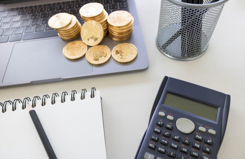Physical cryptocurrency coins resting on a laptop keyboard, next to a calculator and a notepad, symbolizing the planning and growth of fintech.