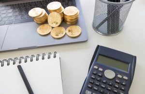 Physical cryptocurrency coins resting on a laptop keyboard, next to a calculator and a notepad, symbolizing the planning and growth of fintech.
