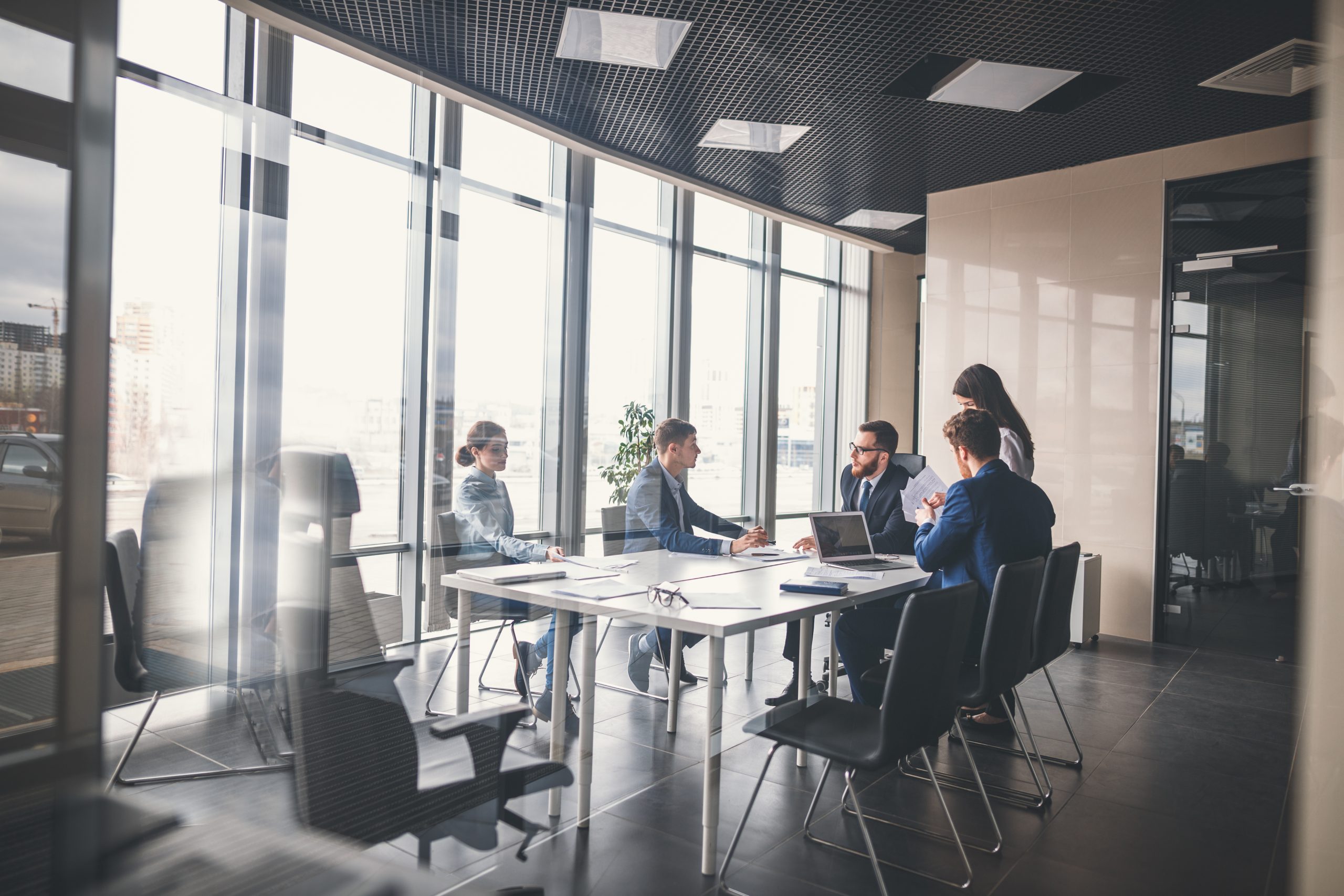 A team of financial professionals sitting around a table in a modern, glass-walled conference room, engaging in a strategic discussion.