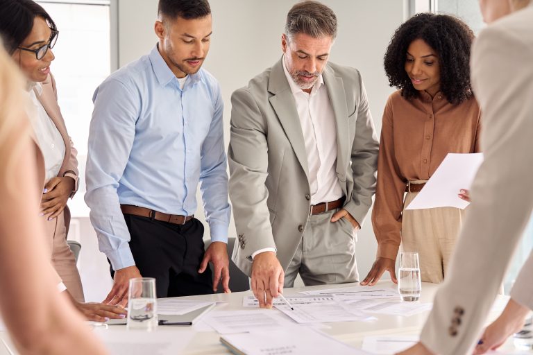 A diverse team of business executives reviewing documents during a strategy meeting, led by a senior manager.