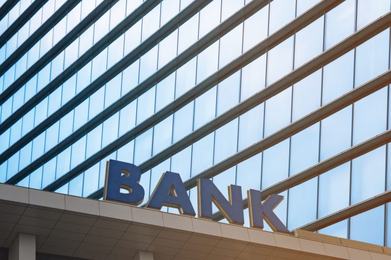 A large blue 'BANK' sign on the exterior of a modern glass office building.
